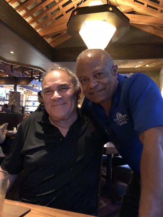 Two friends pose together, smiling, while enjoying dinner at a bustling restaurant.