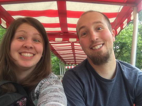 A couple smiles broadly while riding on an amusement park train together, enjoying their outing.