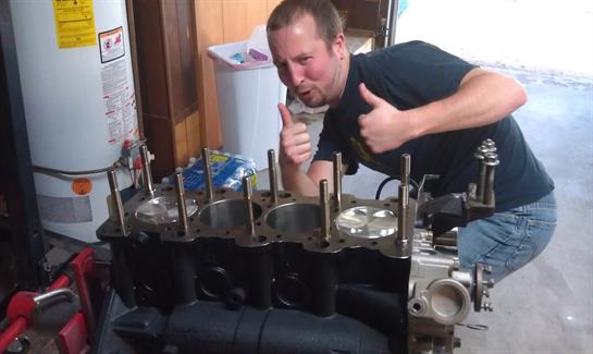 Mechanic proudly poses with an engine block, displaying thumbs up during motor repair work.