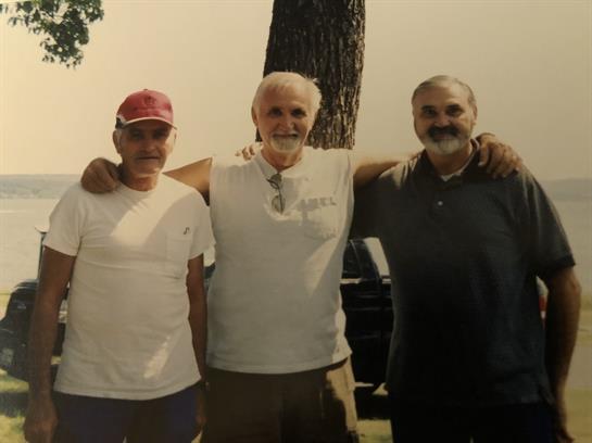 Three friends pose happily together outdoors on a sunny day in a park setting.