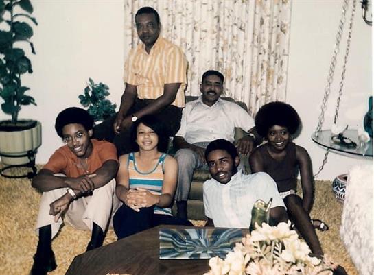 A group of six people, dressed in colorful clothes, enjoy a joyful reunion in a cozy living room.