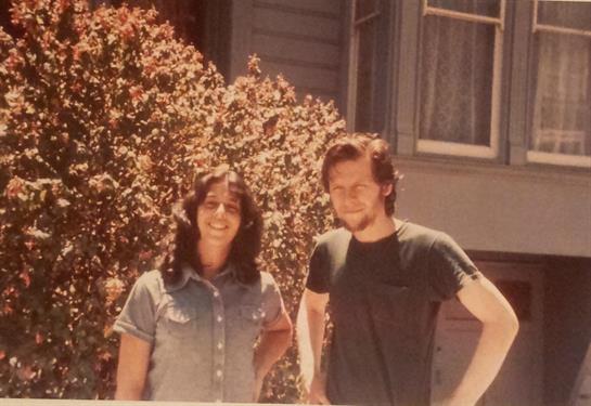 Two smiling individuals stand together outside a home, enjoying a warm, sunny day.