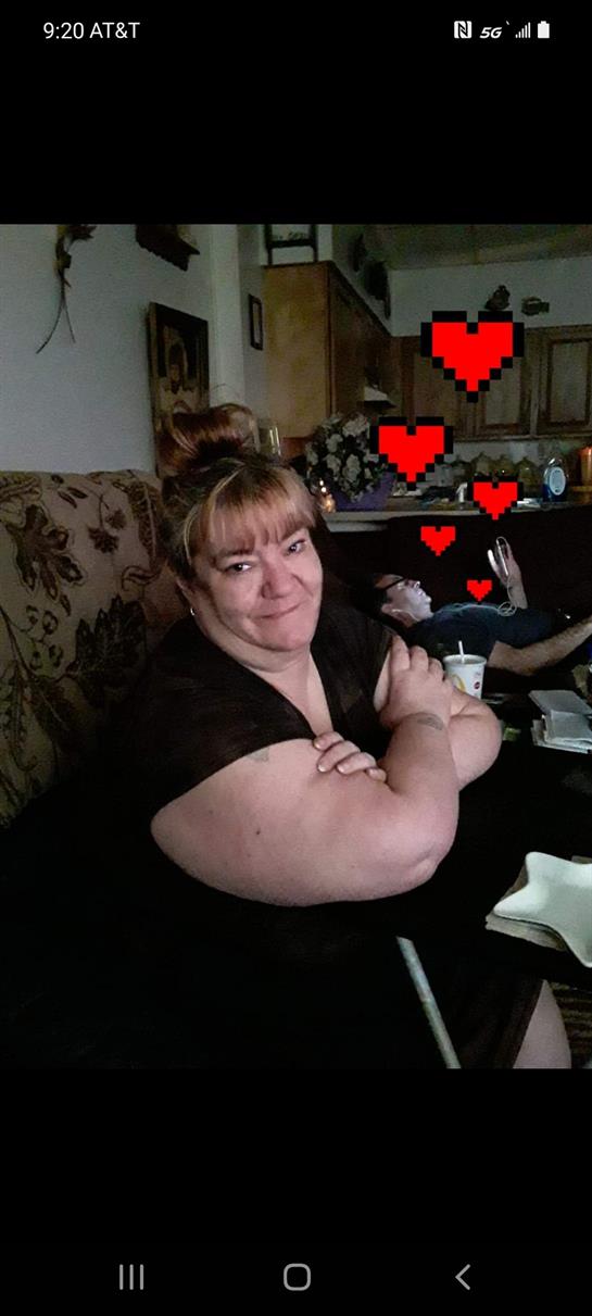 A woman sits comfortably on a couch with her arms crossed, smiling warmly.