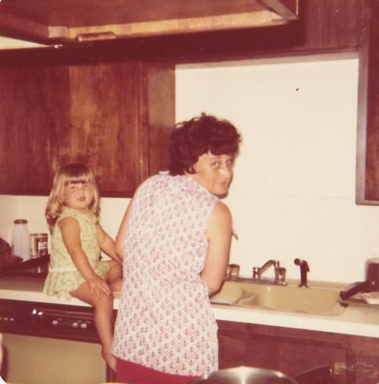 A young girl sits on the kitchen counter as her mother washes dishes, creating a warm family moment.