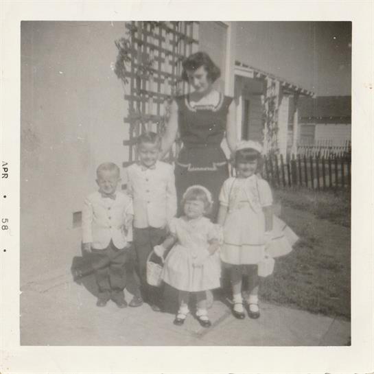 Four children stand in white attire with a woman in a backyard, capturing a moment from the past.