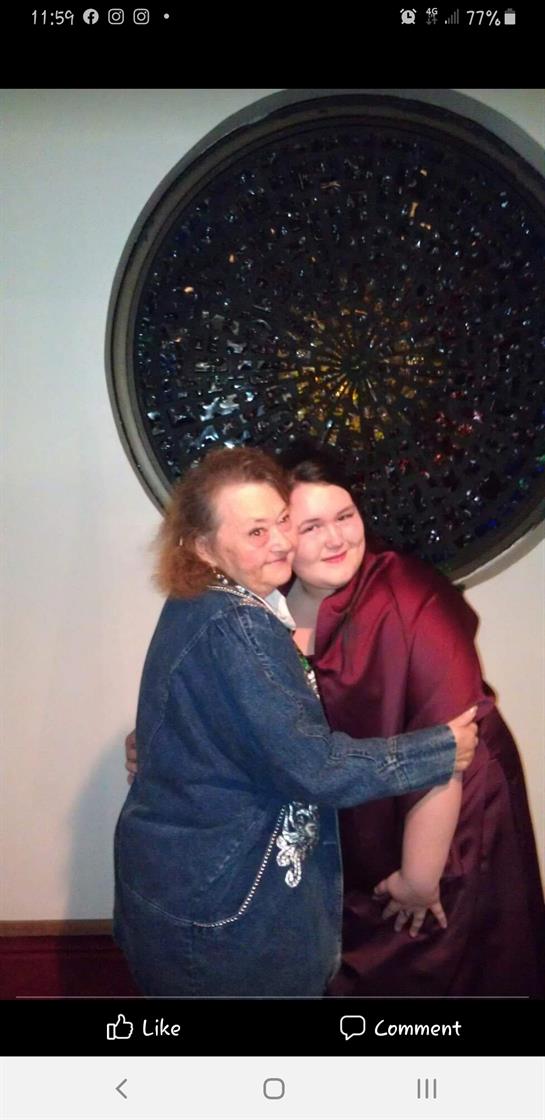 Two women smile and embrace each other in a comfortable indoor environment, showcasing joy.