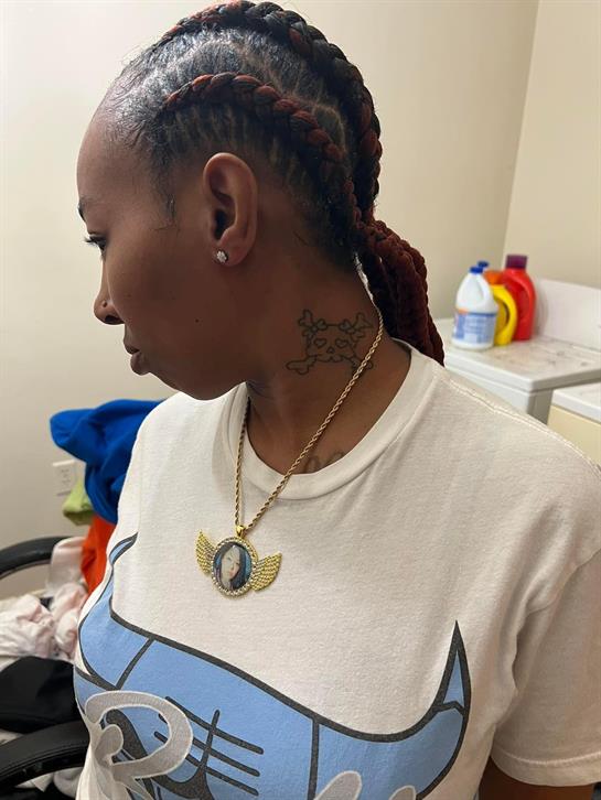 A woman wearing a unique necklace is inside a laundry room with various cleaning supplies visible.