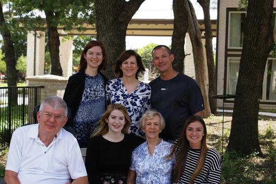 Group of seven family members enjoying time together at a park surrounded by trees.