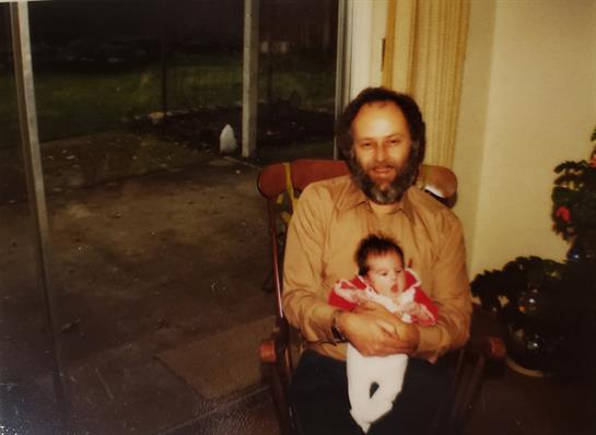 An elderly man gently cradles a newborn baby while sitting indoors, creating a warm moment.