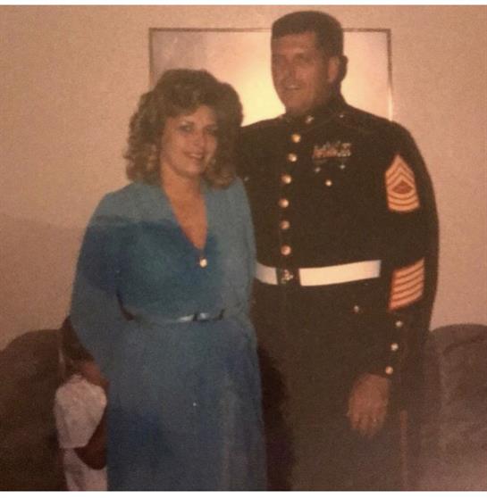 A couple stands close in a cozy living room, smiling as they celebrate together.