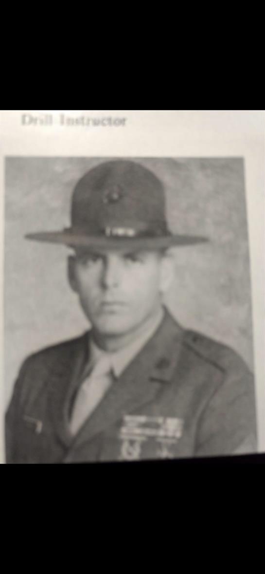 A drill instructor in military uniform poses seriously, wearing a campaign hat and badges.