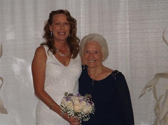 A bride stands beside her grandmother, both smiling warmly at the wedding reception venue.