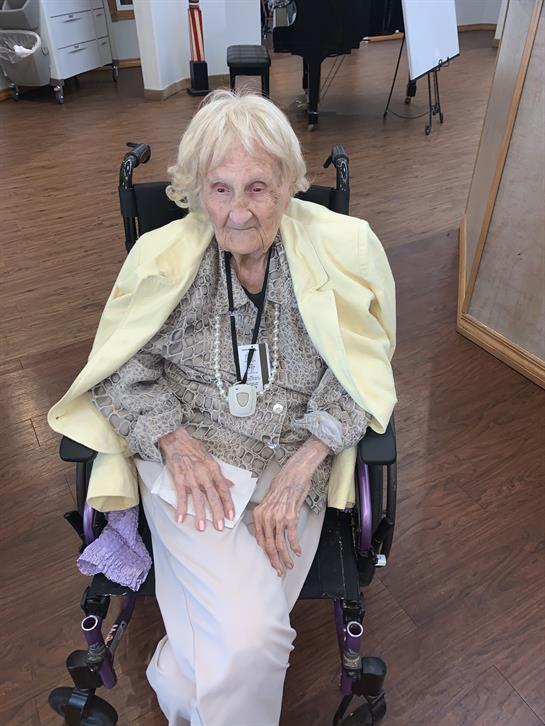 An elderly woman relaxes in a wheelchair wearing a light sweater, engaging in community activities.