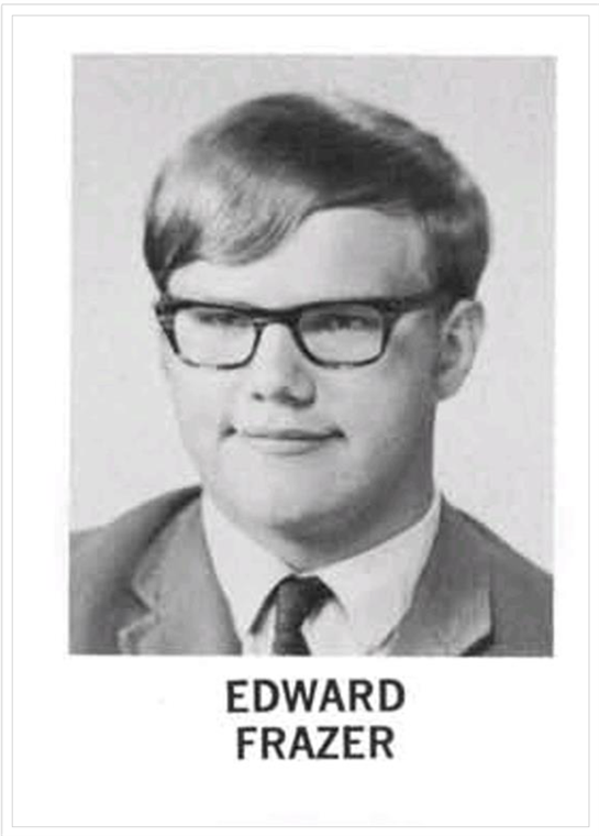 Young man with glasses smiling while wearing a suit and tie, taken during a school photo session.