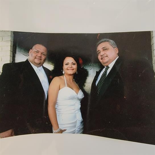 Three friends in formal wear pose happily outdoors for a celebration.