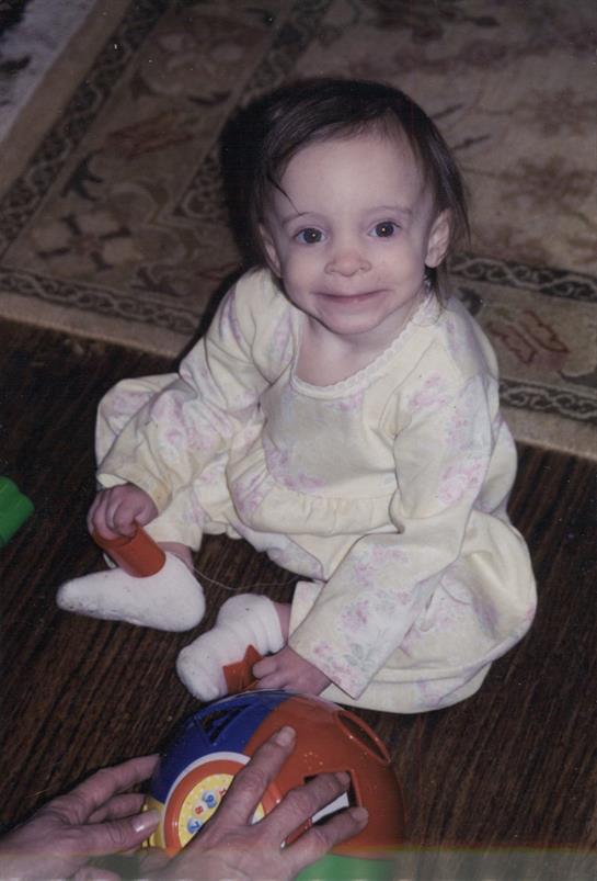 A young child sits on the floor, happily focused on playing with vibrant toys while smiling.