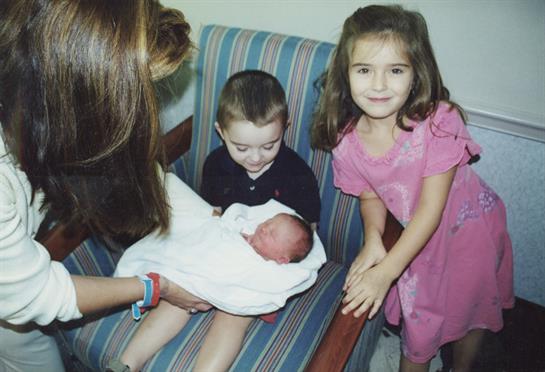 Siblings excitedly surround their newborn brother, sharing smiles and warmth in a cozy setting.