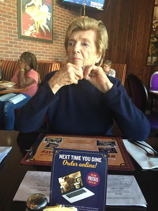 An older woman sits at a restaurant table, deep in thought while reviewing the menu.
