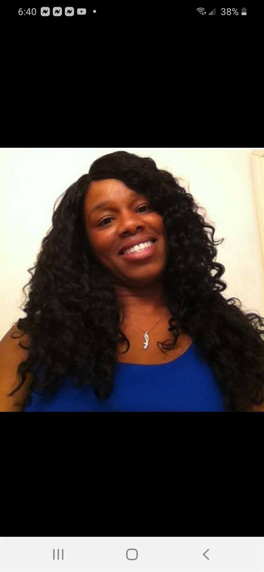 A woman with long curls smiles warmly in a blue top, radiating a friendly vibe.