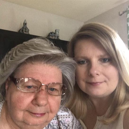Two women pose together, smiling warmly, enjoying a moment in a cozy indoor setting.