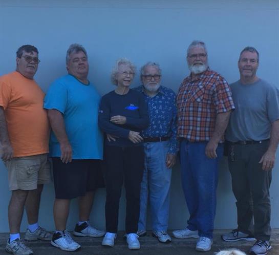 A group of seven friends, smiling and standing together outdoors, enjoying a cheerful moment.