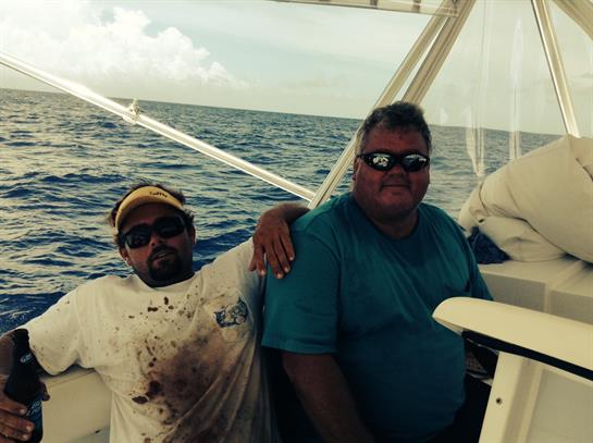 Two fishermen sit on a boat, enjoying their time relaxing on the ocean waves as they fish.