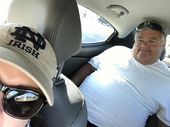 Two friends are sharing a lighthearted moment in a car during bright weather.