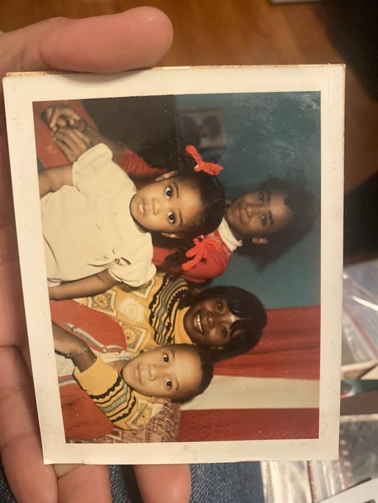 Three children and an adult are smiling together in a vibrant setting, dressed in cheerful outfits.