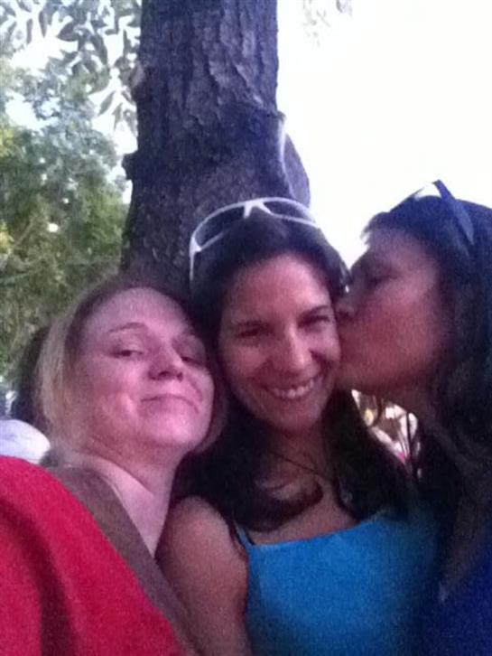 Three friends gather under a tree, laughing and sharing a joyful moment together in the sun.