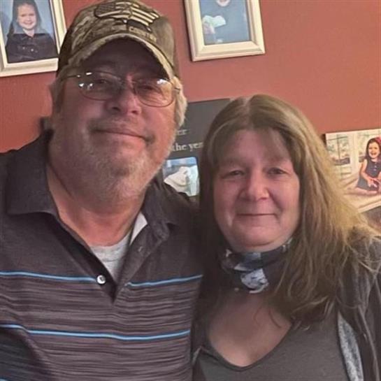 A happy couple stands side by side in a warm indoor environment, smiling at the camera.