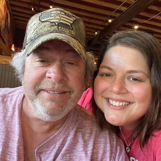 Two friends smile and pose for a selfie inside a cozy restaurant with wooden decor.