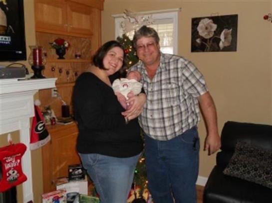 A family celebrates the holidays with their new baby in a cozy, decorated living room.