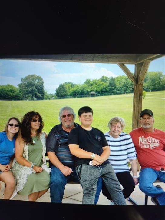 A group of seven people sit together in a park gazebo, enjoying a summer afternoon.