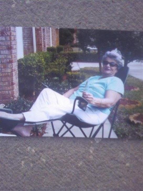 Older woman sits back in a chair, relaxing in a garden while enjoying the sunshine.