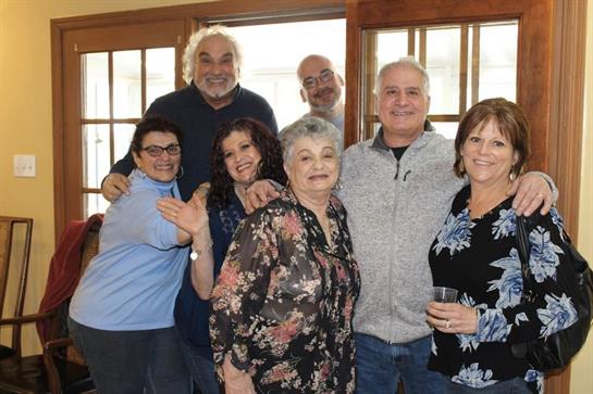 A joyful group of eight friends celebrates together indoors, smiling and sharing good memories.