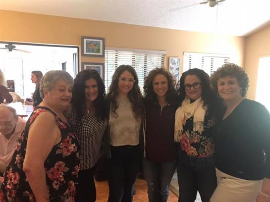 A joyful gathering of women smiling and posing together in a warm, well-lit room.
