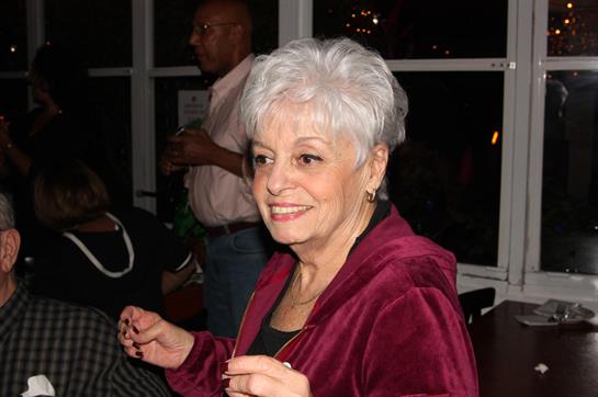 Smiling woman with silver hair enjoys a lively moment at a social gathering in the evening.