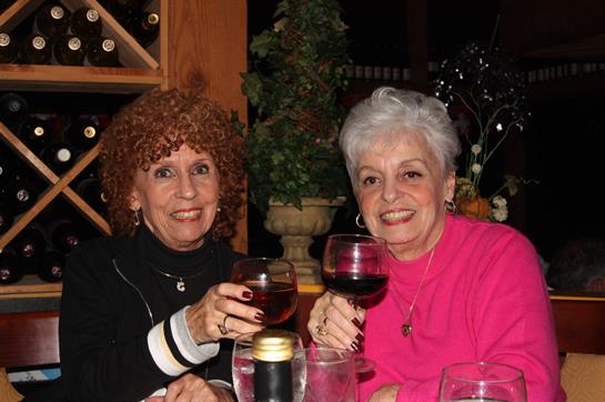 Two women smile and raise their glasses in a warm atmosphere, celebrating friendship and good times.