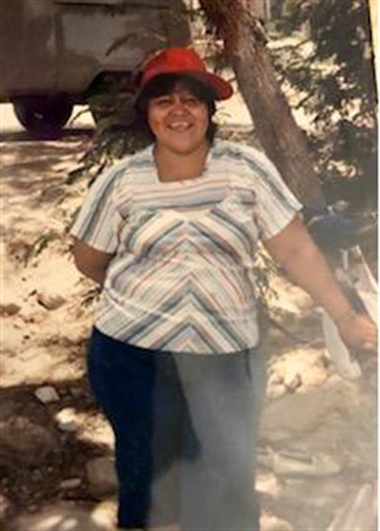 A woman in casual clothes smiles outdoors by a tree on a sunny day.