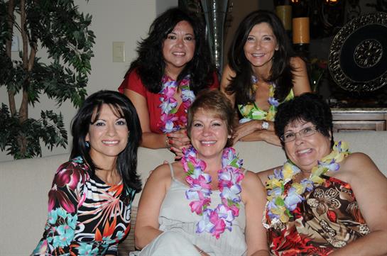 Group of friends enjoying a festive gathering, wearing colorful clothing and leis, smiling brightly.