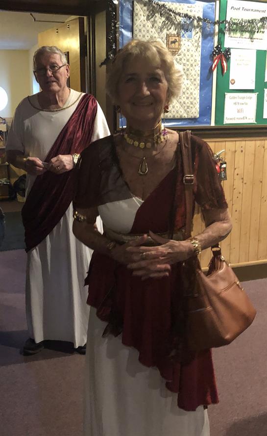 Two women in traditional Roman costumes participate in a community gathering, smiling and engaging.