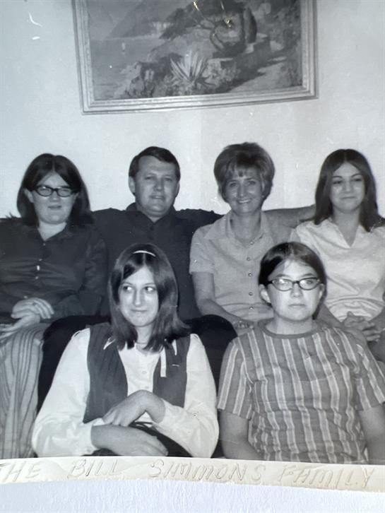 A group of six family members sit comfortably together in a living room, enjoying their time.