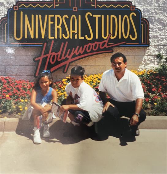 A child and an adult smile in front of the Universal Studios Hollywood sign with flowers.