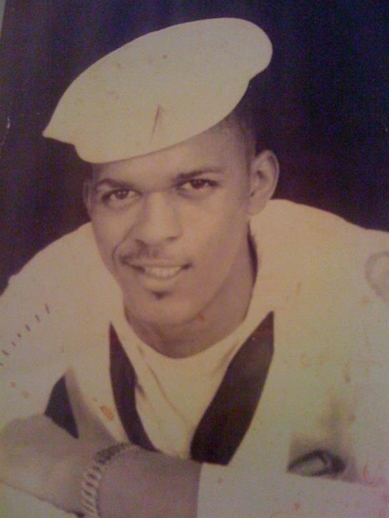 A young sailor smiles while wearing a navy uniform and cap, showcasing pride and camaraderie.