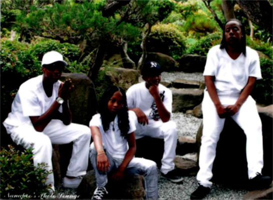 Five friends dressed in white sit and stand among greenery, enjoying a peaceful moment outdoors.