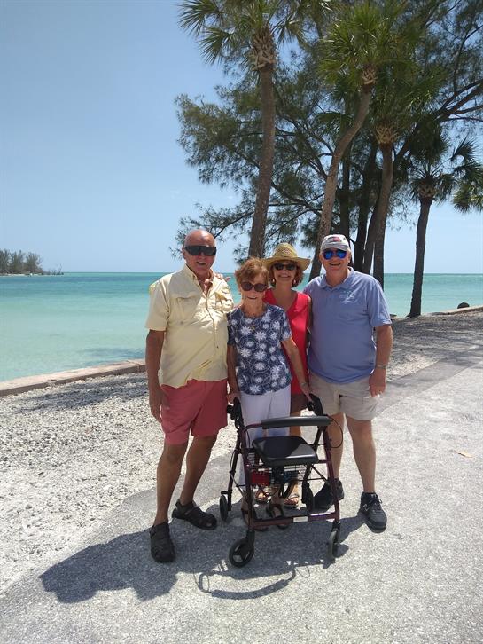 Four individuals stand by the shore, enjoying the warm weather and beautiful ocean view.