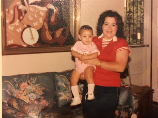 Woman smiles while holding a baby in a cozy living room filled with vintage decorations.