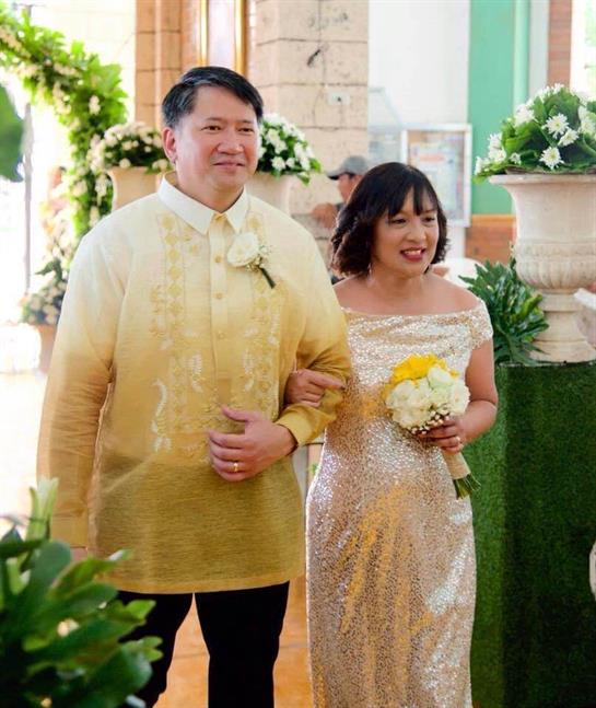 A man in traditional attire escorts a woman in elegant dress holding a bouquet.