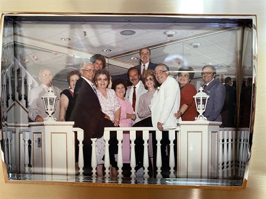Groups of people celebrate a joyful occasion on a cruise deck, dressed in formal attire.