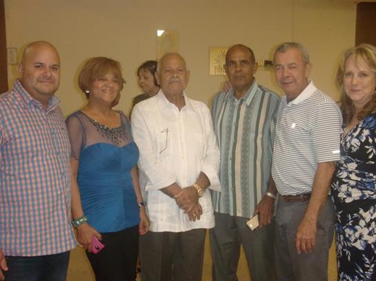 Five individuals stand together, smiling in a community center during an evening gathering.